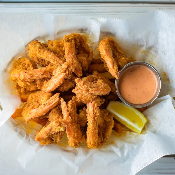 A basket of Ben's Crab fried shrimp with a side of sauce and a lemon wedge.