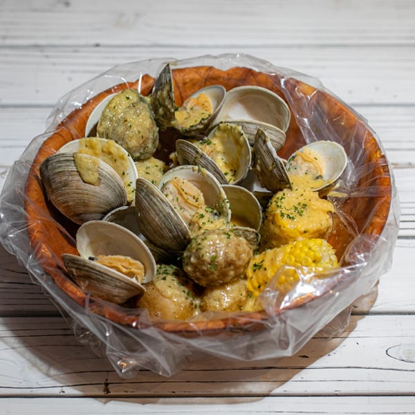 Steamed clams, potatoes, and corn on the cob in a plastic bag, seasoned with herbs and sauce.