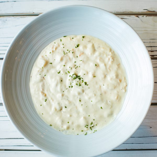 Creamy seafood chowder, garnished with fresh herbs, served in a white bowl on a light wooden table.