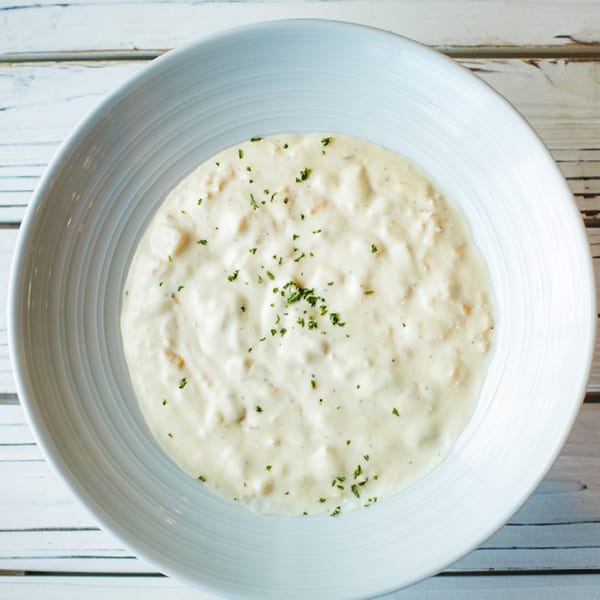 Creamy seafood chowder, garnished with parsley, in a white bowl on a light wooden table.