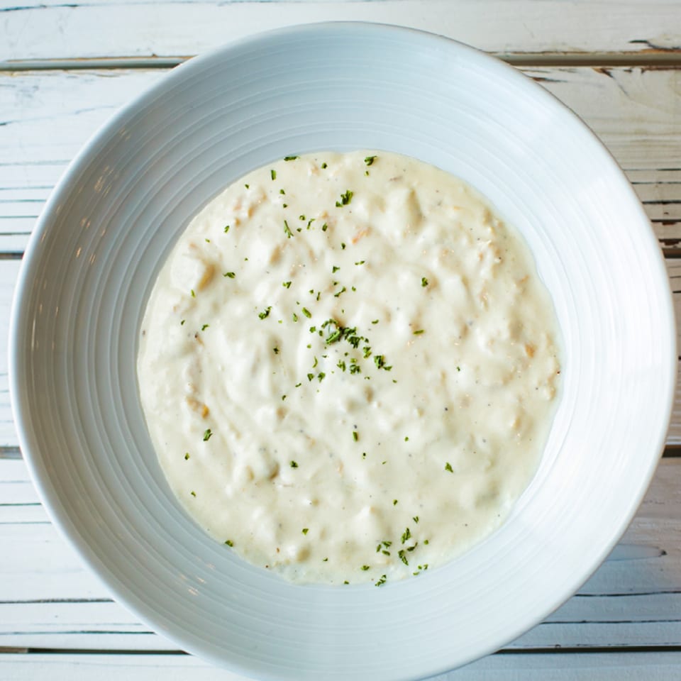 Creamy seafood chowder, garnished with parsley, in a white bowl on a light wooden table.