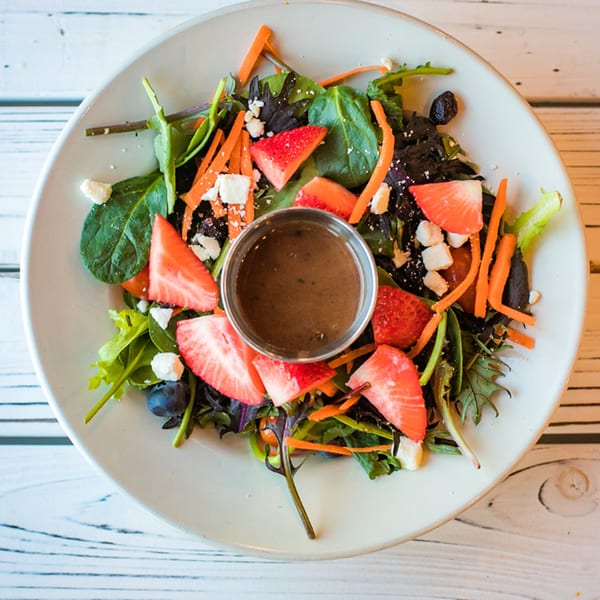 Overhead view of a fresh salad with mixed greens, strawberries, carrots, blueberries, and feta cheese.