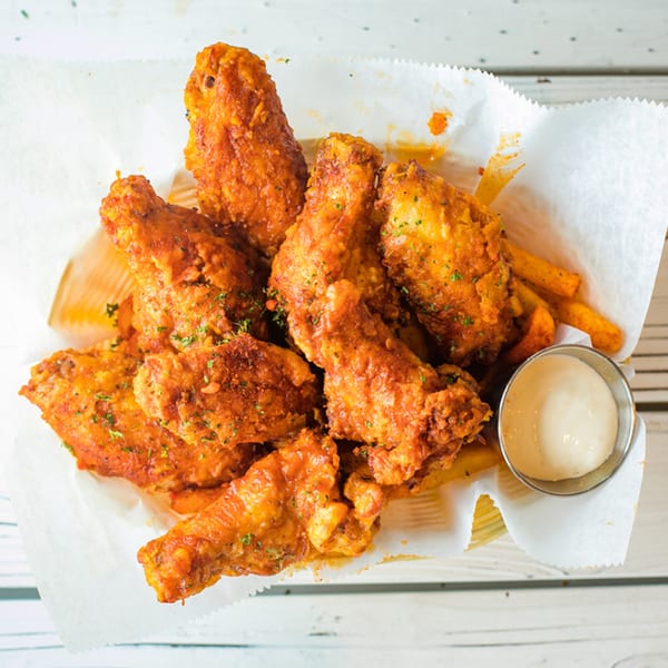 Ben's Crab fried chicken wings with fries and dipping sauce in a basket on a white wooden table.