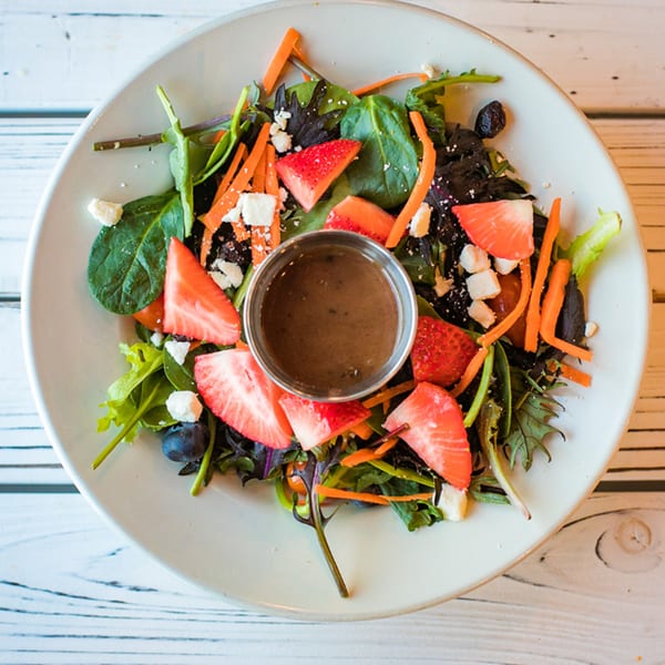 Overhead view of a fresh salad with strawberries, blueberries, carrots, and feta cheese.
