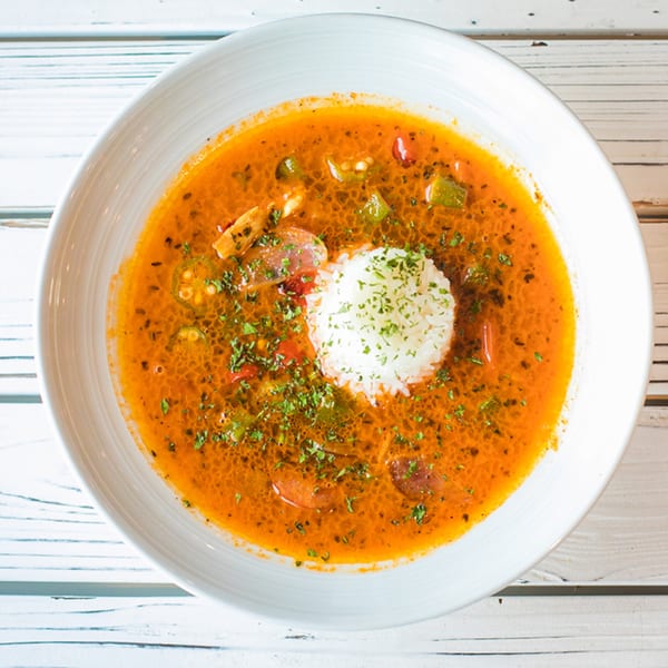 Ben's Crab seafood gumbo, a rich orange stew with rice, sausage, and vegetables in a white bowl.