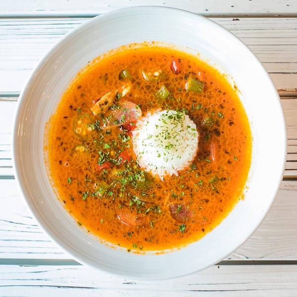 Ben's Crab seafood gumbo with rice and parsley in a white bowl on a wooden table.
