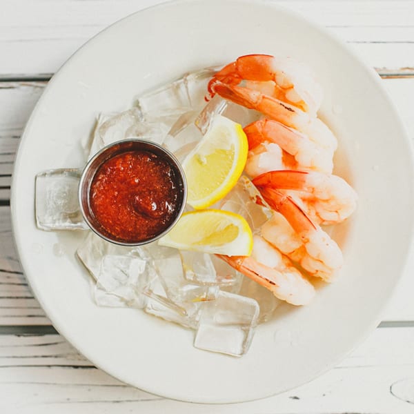 Shrimp cocktail with lemon wedges and red sauce on a bed of ice, on a white plate.