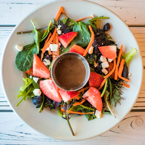 Overhead view of a fresh salad with strawberries, blueberries, carrots, and feta cheese.