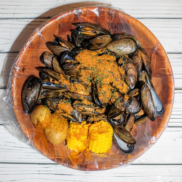 Ben's Crab mussels in a wooden bowl with corn and potatoes, covered in a rich sauce.