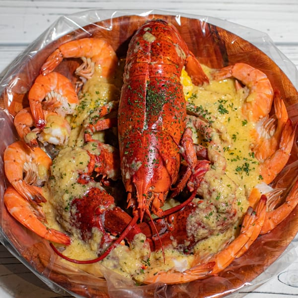 A large wooden bowl filled with Ben's Crab seafood boil, including lobster, shrimp, and corn.