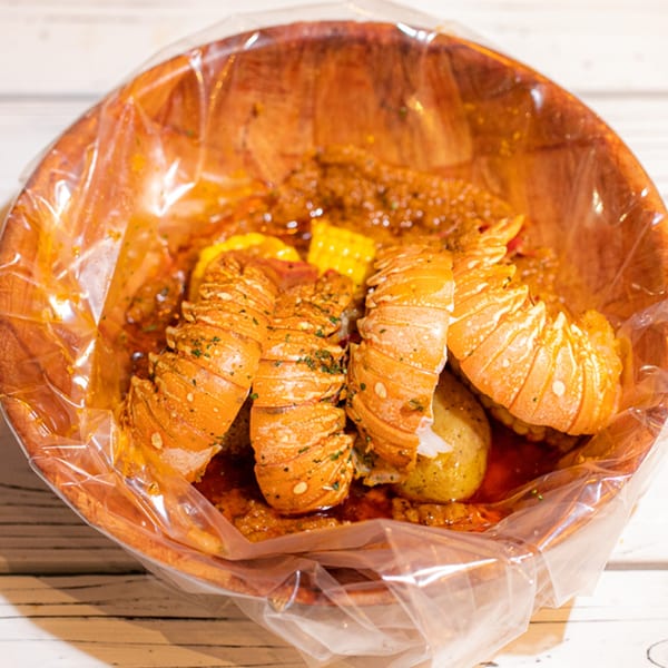Ben's Crab lobster tails, corn, and potatoes in a wooden bowl lined with a plastic bag.