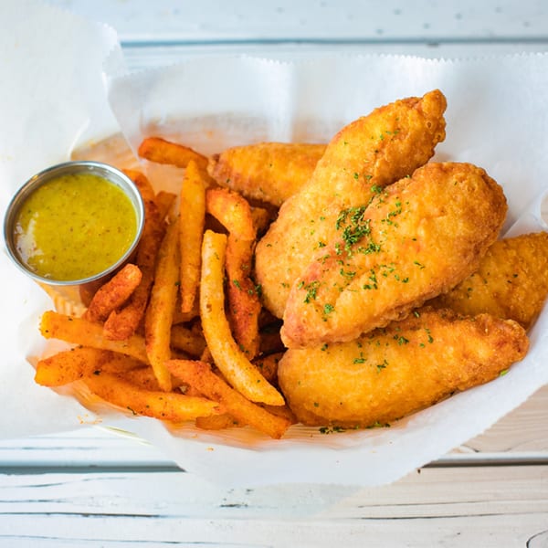 Golden fried fish fillets and seasoned fries with a side of green dipping sauce in a basket.