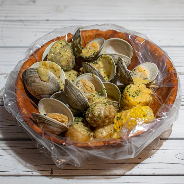 Steamed clams, potatoes, and corn on the cob in a wooden bowl, covered in a creamy sauce.