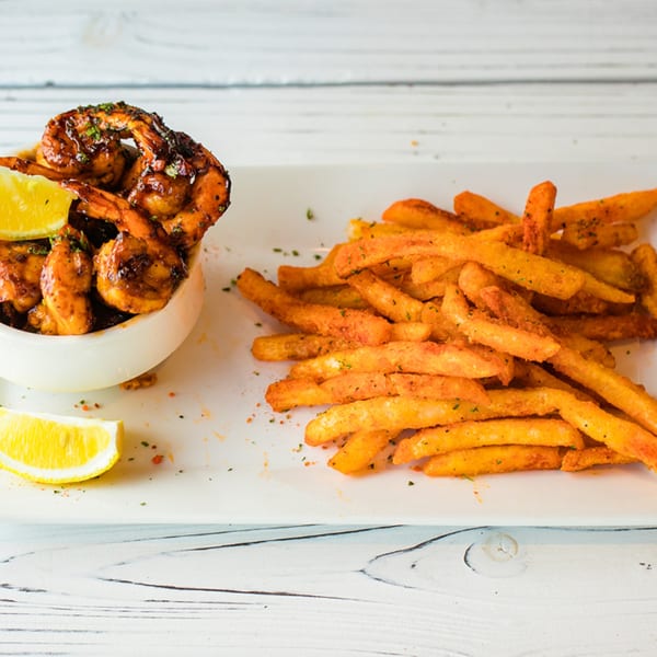 Ben's Crab spicy shrimp with lemon wedges and a side of seasoned french fries on a white plate.