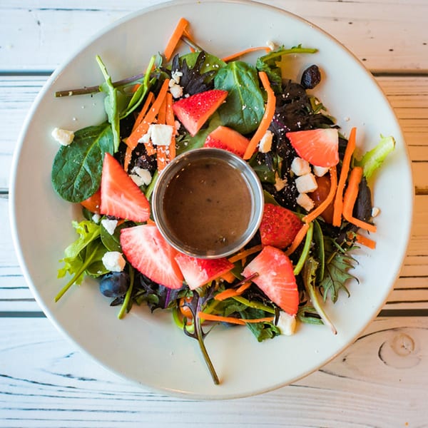 A vibrant salad with mixed greens, strawberries, blueberries, carrots, feta cheese, and a side of dressing.