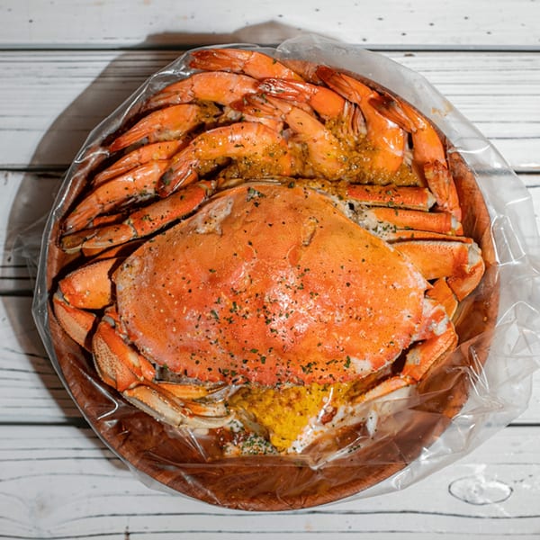 Ben's Crab seafood boil with a whole crab and shrimp in a clear bag on a wooden platter.