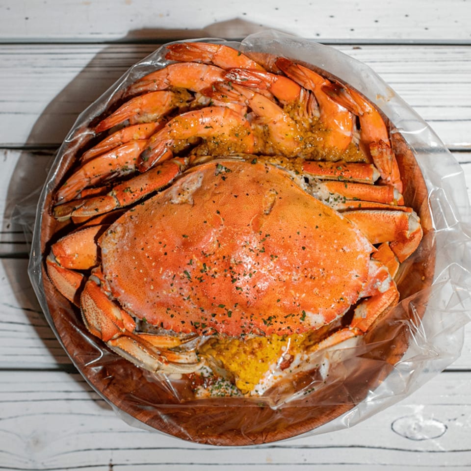 Ben's Crab seafood boil with a whole crab and shrimp in a clear bag on a wooden platter.