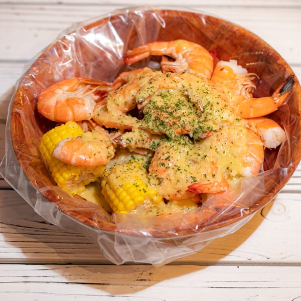Ben's Crab seafood boil with shrimp, corn on the cob, and sauce in a wooden bowl.