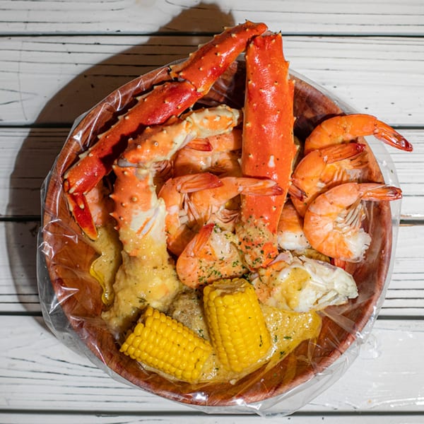 Ben's Crab seafood boil with crab legs, shrimp, corn on the cob, and sauce in a wooden bowl.
